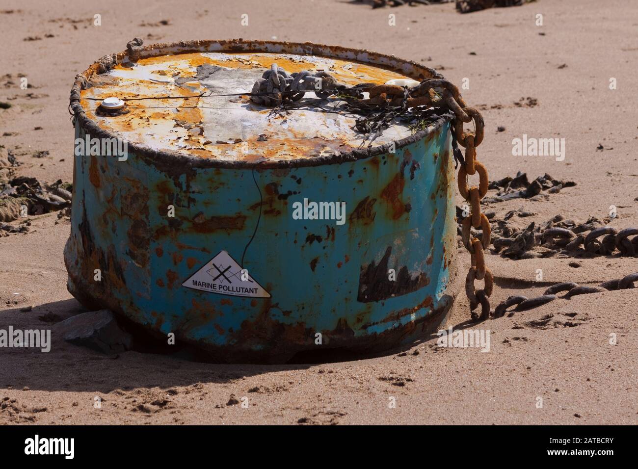Marine pollutant barrel buried in sand on a UK beach. Pollution is a large contributor to global warming. Stock Photo
