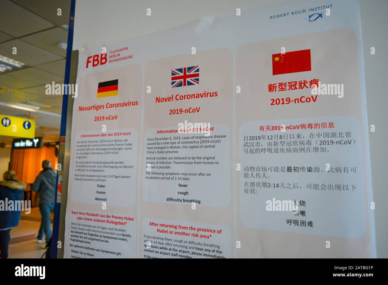 Berlin Schonefeld Airport SXF, Germany - 02/01/20: Warning sign advises about Coronavirus 2019-nCoV to all airport travellers. Written in German, English and Chinese language. Background with passengers in Berlin Airport Stock Photo