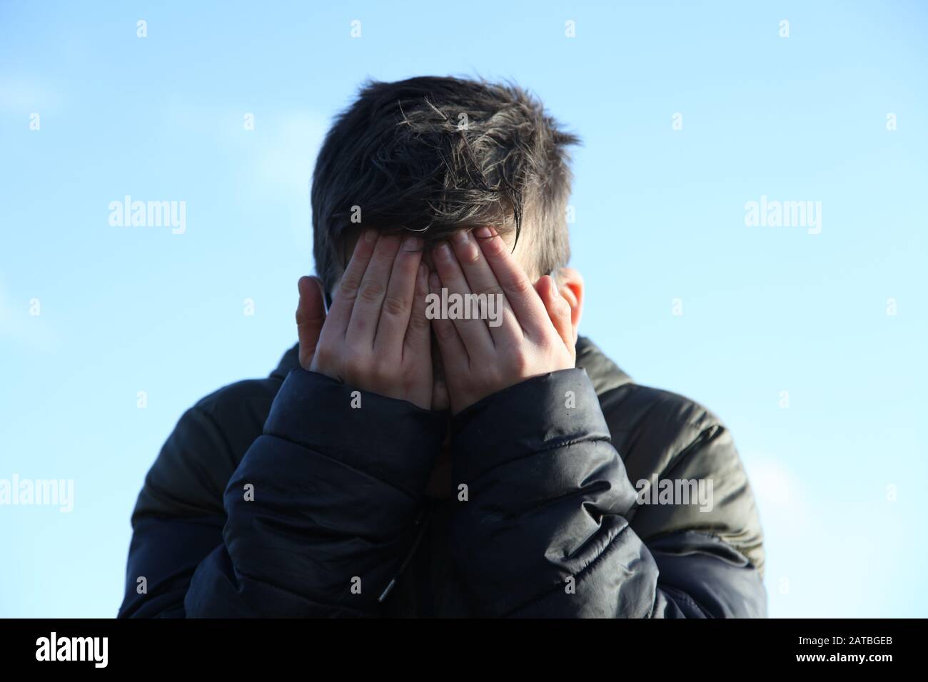 A young boy of 12 covers his muddy face with his hands, facing camera Stock Photo