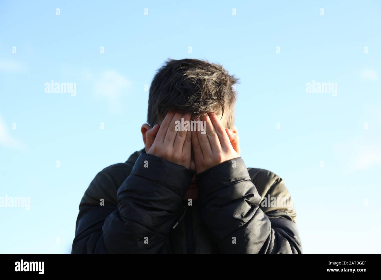 A young boy of 12 covers his muddy face with his hands, facing camera Stock Photo