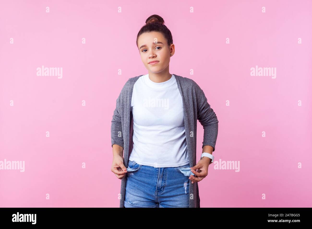 Portrait of frustrated brunette teenage girl with bun hairstyle in casual clothes showing empty pockets inside out, poor has no money, allowance. indo Stock Photo