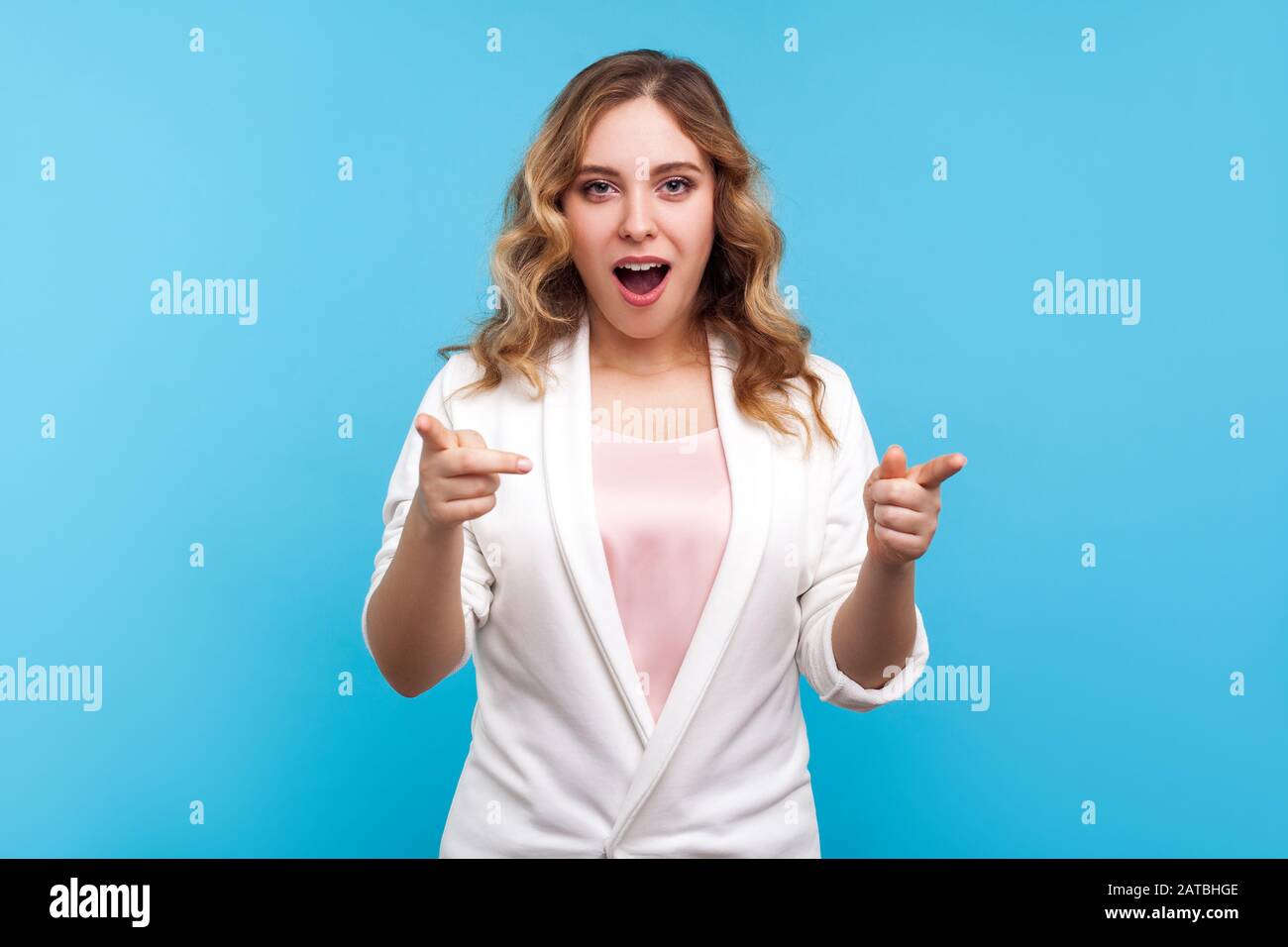 Hey, you are awesome! Portrait of pleasantly surprised woman with wavy hair in white jacket pointing at camera with shocked face, amazed about you. in Stock Photo
