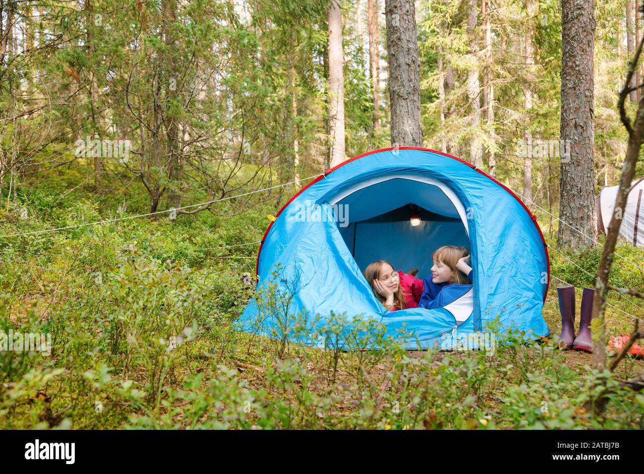 Tween girls lying together in tent chatting while camping in a summer forest during summer holidays Stock Photo