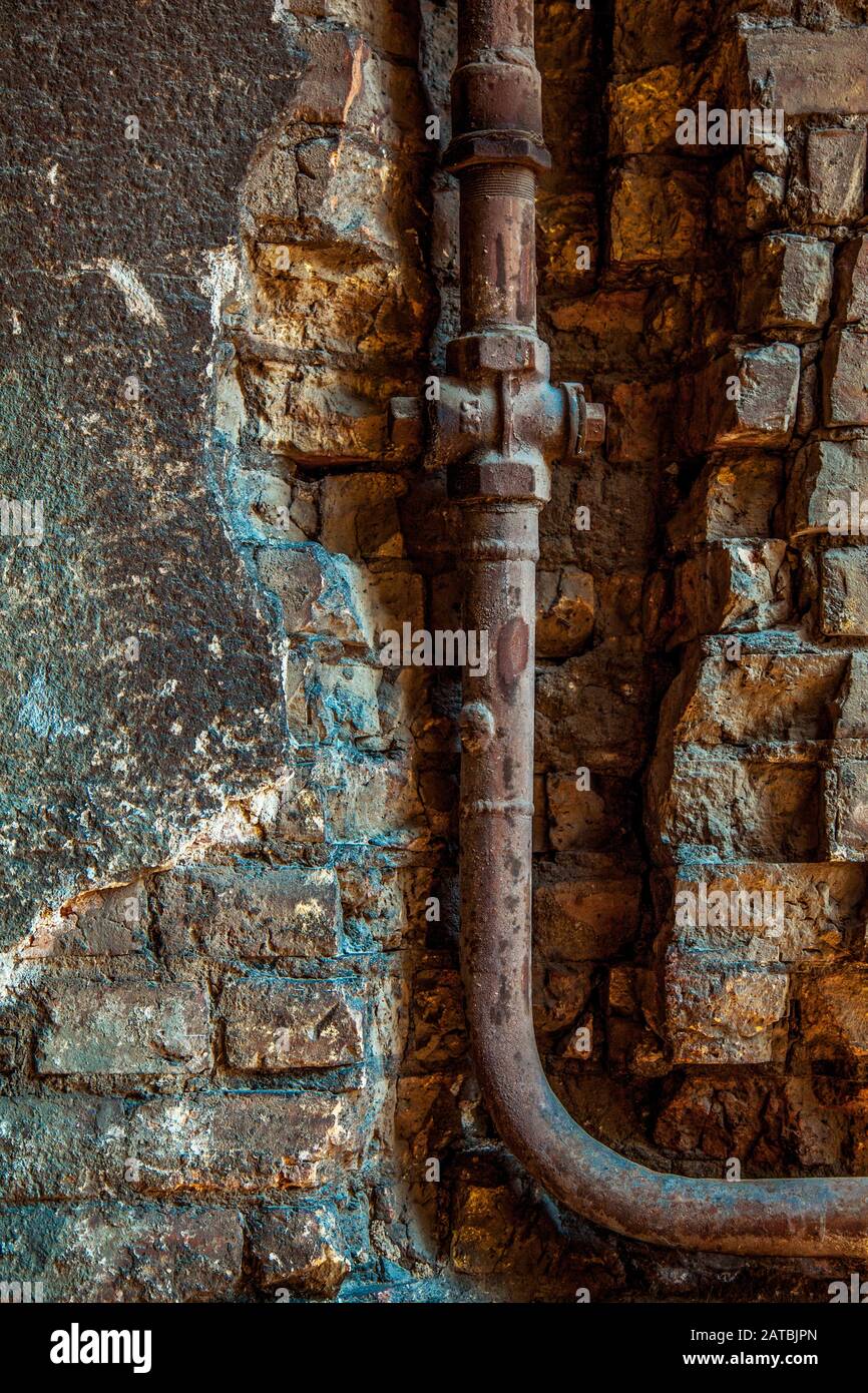 Old rusty water pipe in a brick wall. Old rusty pipe with valves on