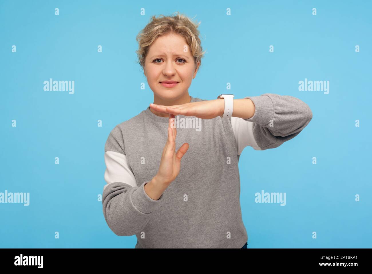 Frustrated woman with short curly hair in grey sweatshirt feeling tired and overworked, showing timeout gesture, need more time, missing deadline. ind Stock Photo