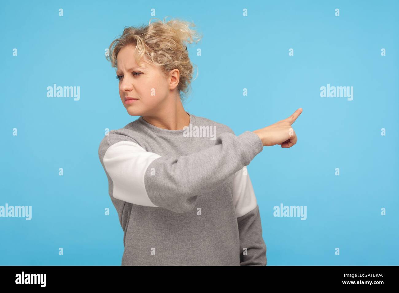 Leave me! Resentful woman with curly hair in sweatshirt pointing sideways, showing get out gesture, ordering to go away, feeling annoyed and vexed. in Stock Photo