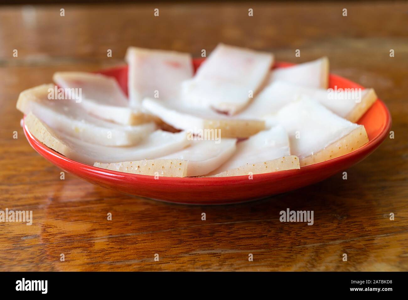 The Bit fat porks on table. The Red plate on wooden table.Salty white slices Stock Photo