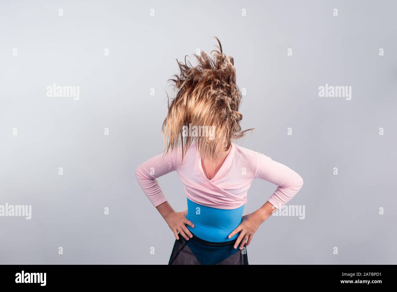 Cheerful teenage girl in pink and blue ballet outfit waving long blond hair which is covering her face. isolated on grey background Stock Photo