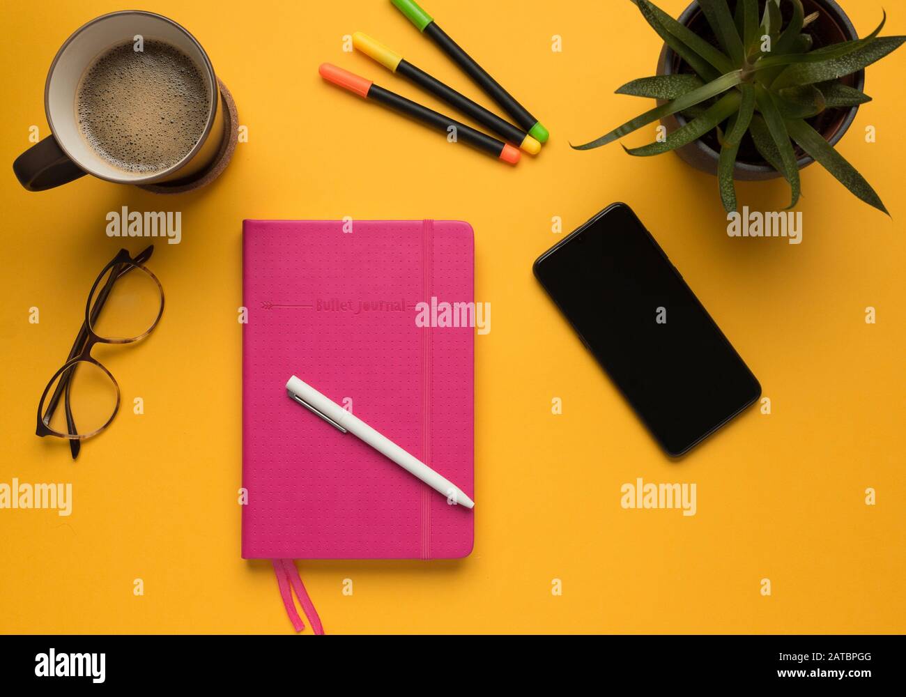 Stock photo of a pink diary with pencil, smartphone and some desktop objects on a yellow background Stock Photo