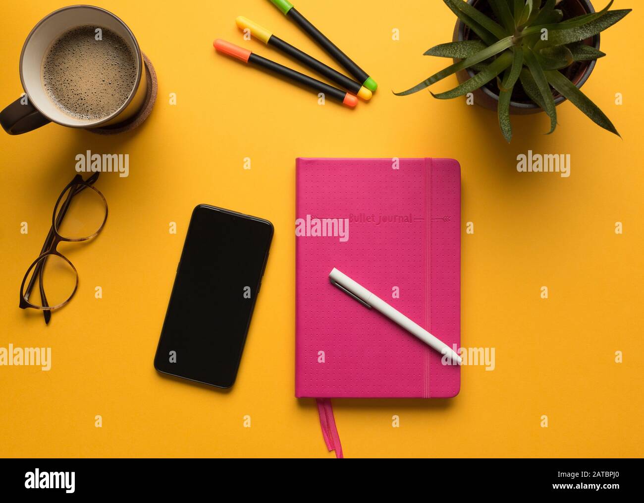 Stock photo of a pink diary with pencil, mobile phone and some desktop objects on a yellow background Stock Photo