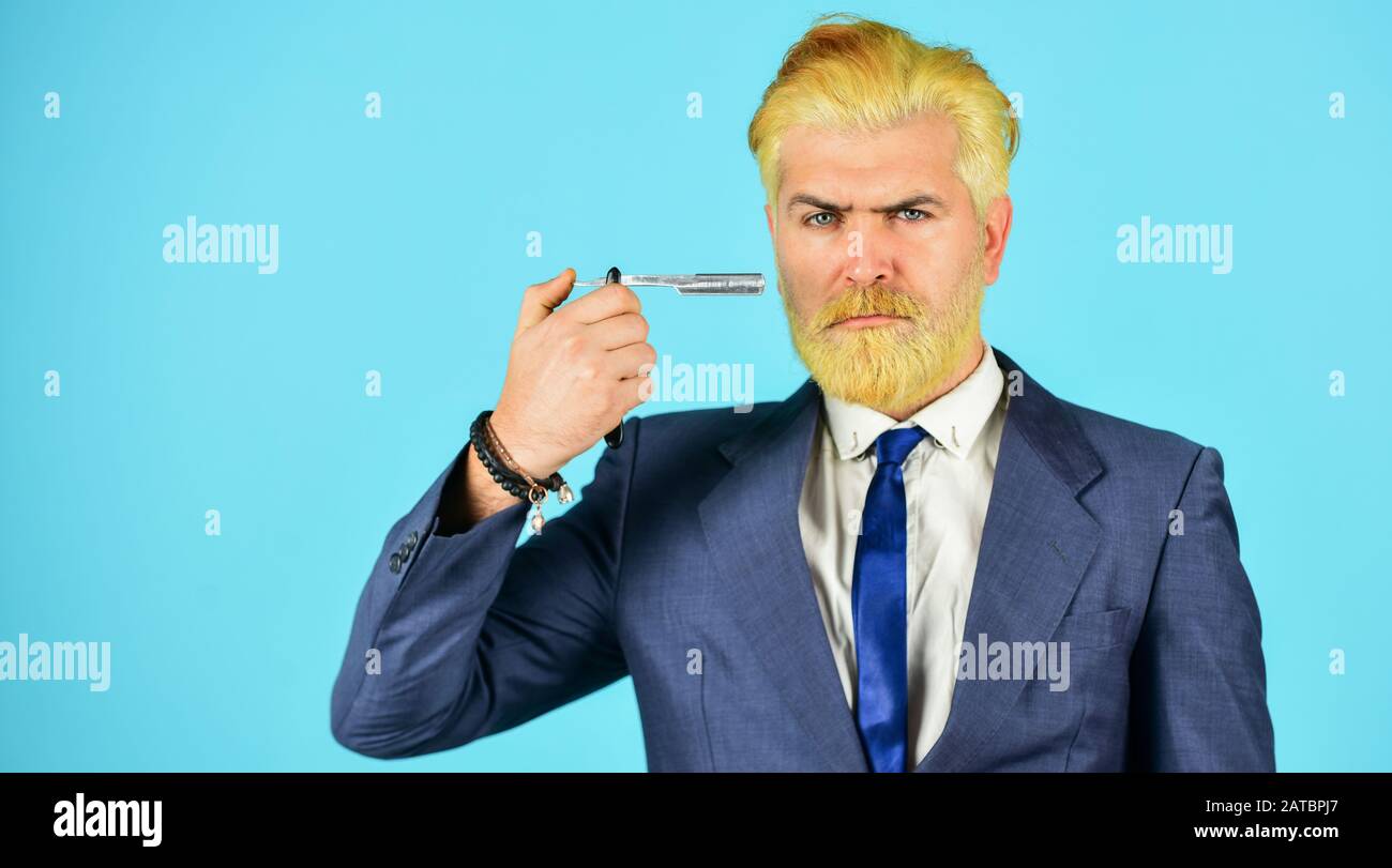 Designing haircut. Fresh hairstyle. Barbershop concept. Barbershop salon. Blond color. Bleached hair. Personal stylist barber. Bearded man hold razor scissors. Retro barbershop. Hipster with tools. Stock Photo
