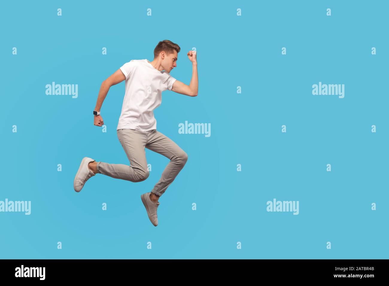 Full length, motivated man in white t-shirt and casual pants running in air with serious confident determined expression, hurrying to meet dream, goal Stock Photo