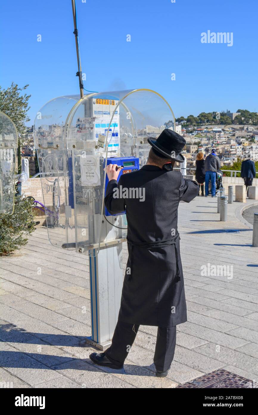 An orthodox jew man is calling from a public payphone in Jerusalem, Israel. Dressed with a hasidic garb. In front of him the view over hills of East Stock Photo