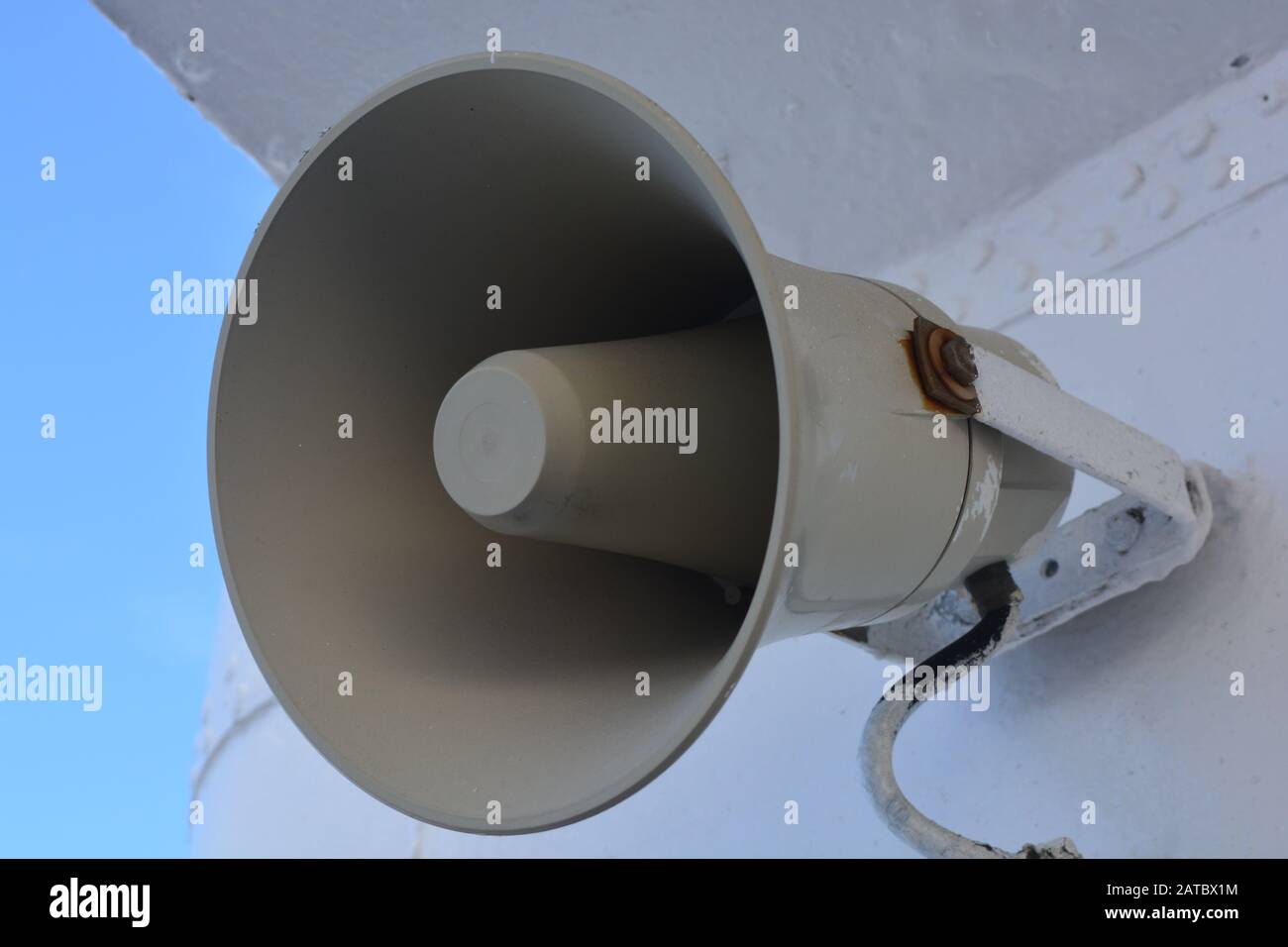 A closeup of a gray loudspeaker hanging from a metal wall. Announcments are made from a megaphone for public attention and safety. Vinage horn speaker Stock Photo