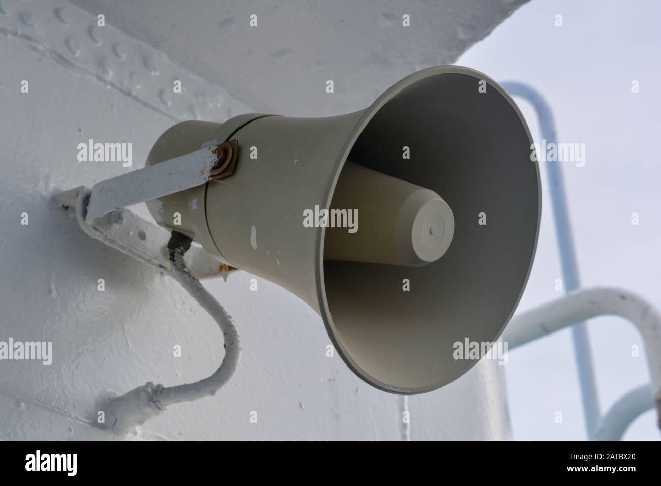 A closeup of a grey loudspeaker hanging from a metal wall. Allerts are sent from a megaphone for public attention and safety. Vintage horn speaker Stock Photo