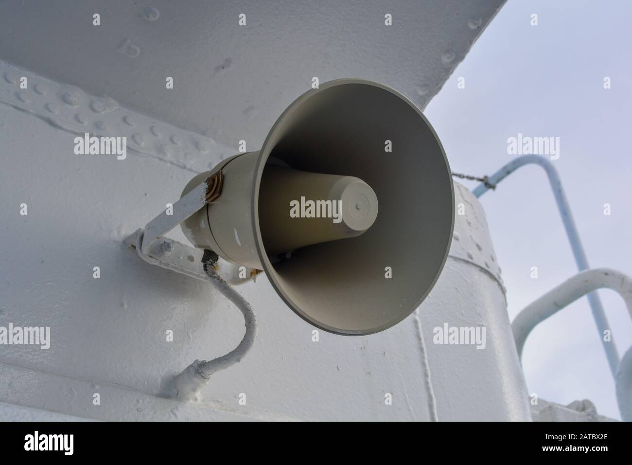 A closeup of a gray loudspeaker hanging from a metal wall. Announcments are made from a megaphone for public attention and safety. Vinage horn speaker Stock Photo