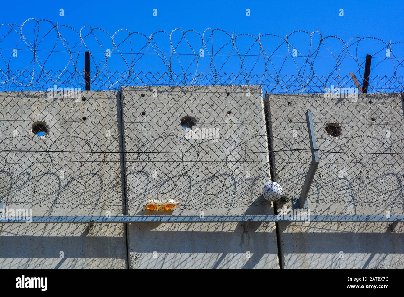 A closeup of the gray concrete separation wall between Israel and Palestine. A ball and a bottle from kids in the West Bank caught in the barbed wire Stock Photo