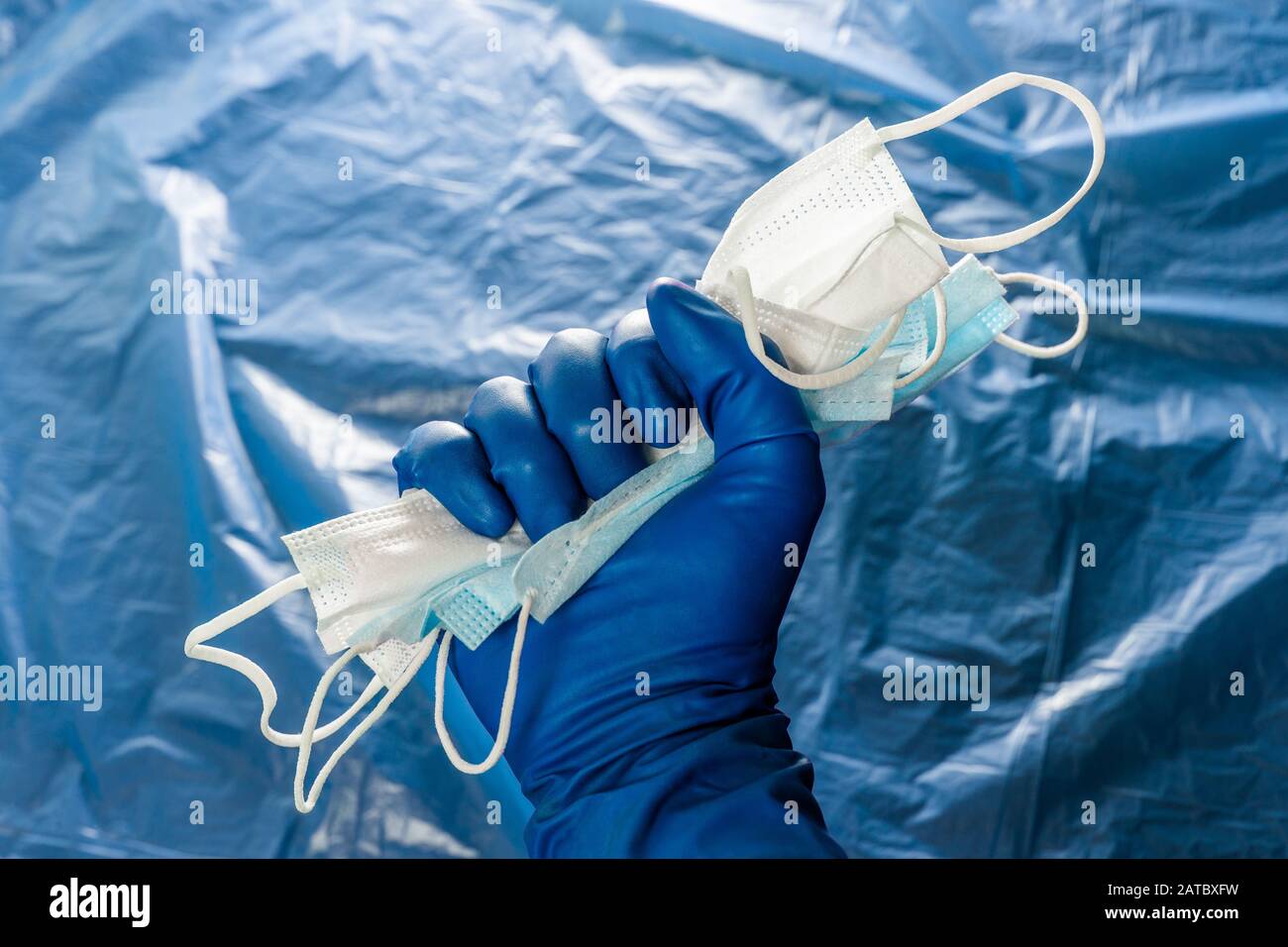 A hand in blue medical glove holding a bunch of face masks on blurry plastic film background. Symbol of coronavirus pandemic resistance and help. Stock Photo