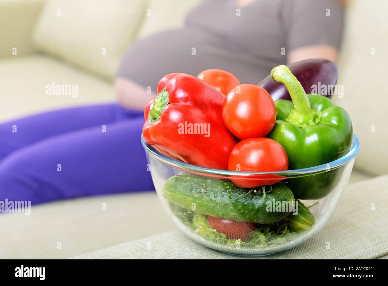 Fresh vegetables on the couch next to a pregnant woman at home Stock Photo