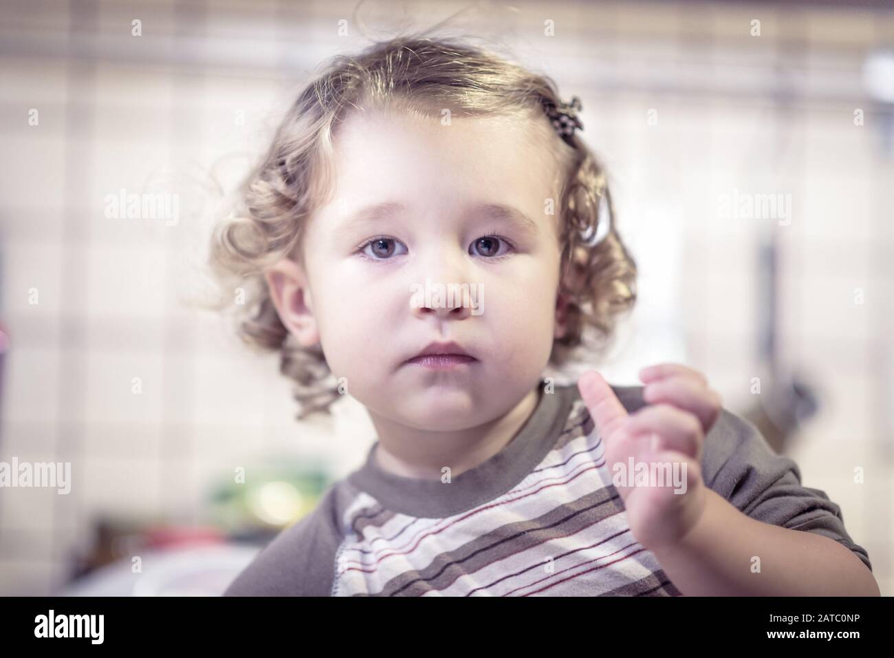 Cute two-year-old girl washes the dishes in kitchen. Little child is posing for a photo. Stock Photo