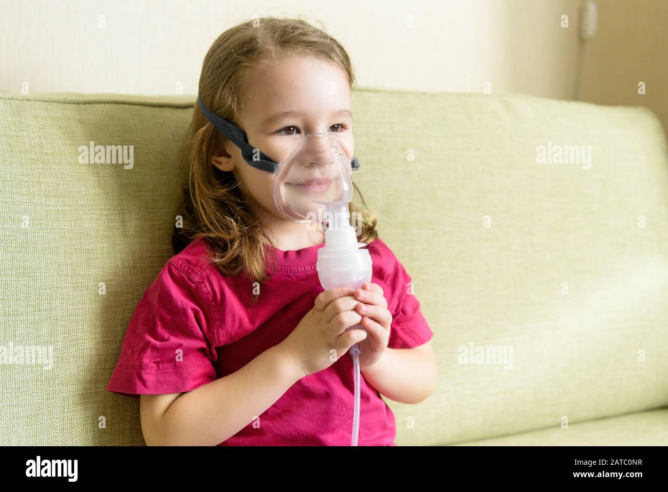 Little girl holds inhaler mask at home. Sick kid breathes through a nebulizer. Baby using equipment to treat asthma or bronchitis. Concept of treatmen Stock Photo