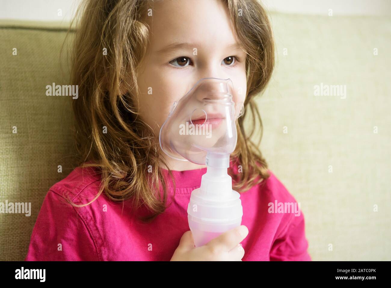 Little girl holds inhaler mask at home. Sick kid breathes through a nebulizer. Baby using equipment to treat asthma or bronchitis. Concept of treatmen Stock Photo