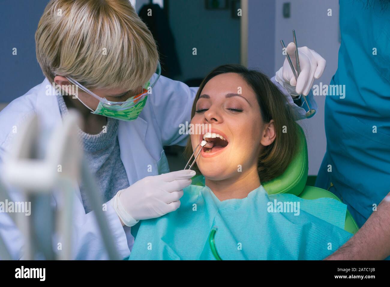 Professional male and female dentists examining woman's teeth in dental ...