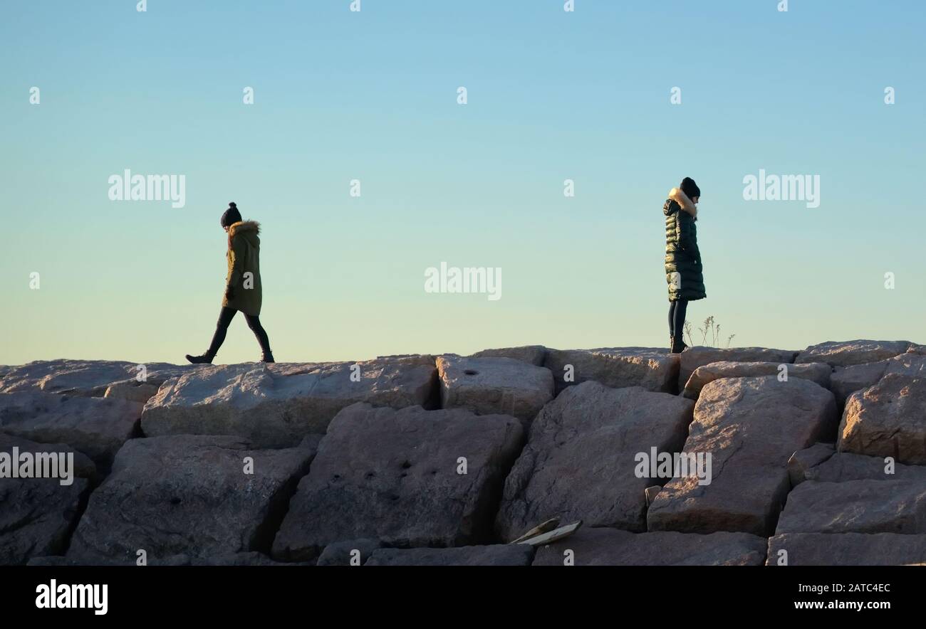 Two young women in winter clothing on boulder walkway walking away from each other. Stock Photo