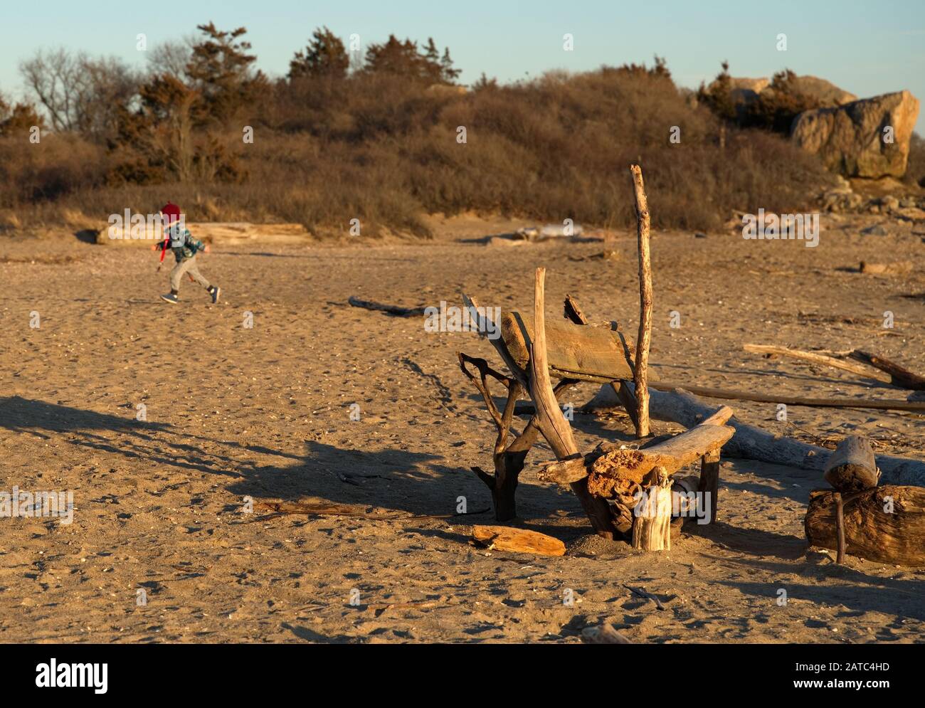 Crude bench made out of washed up logs and driftwood on New England beach with kid in background playing. Stock Photo