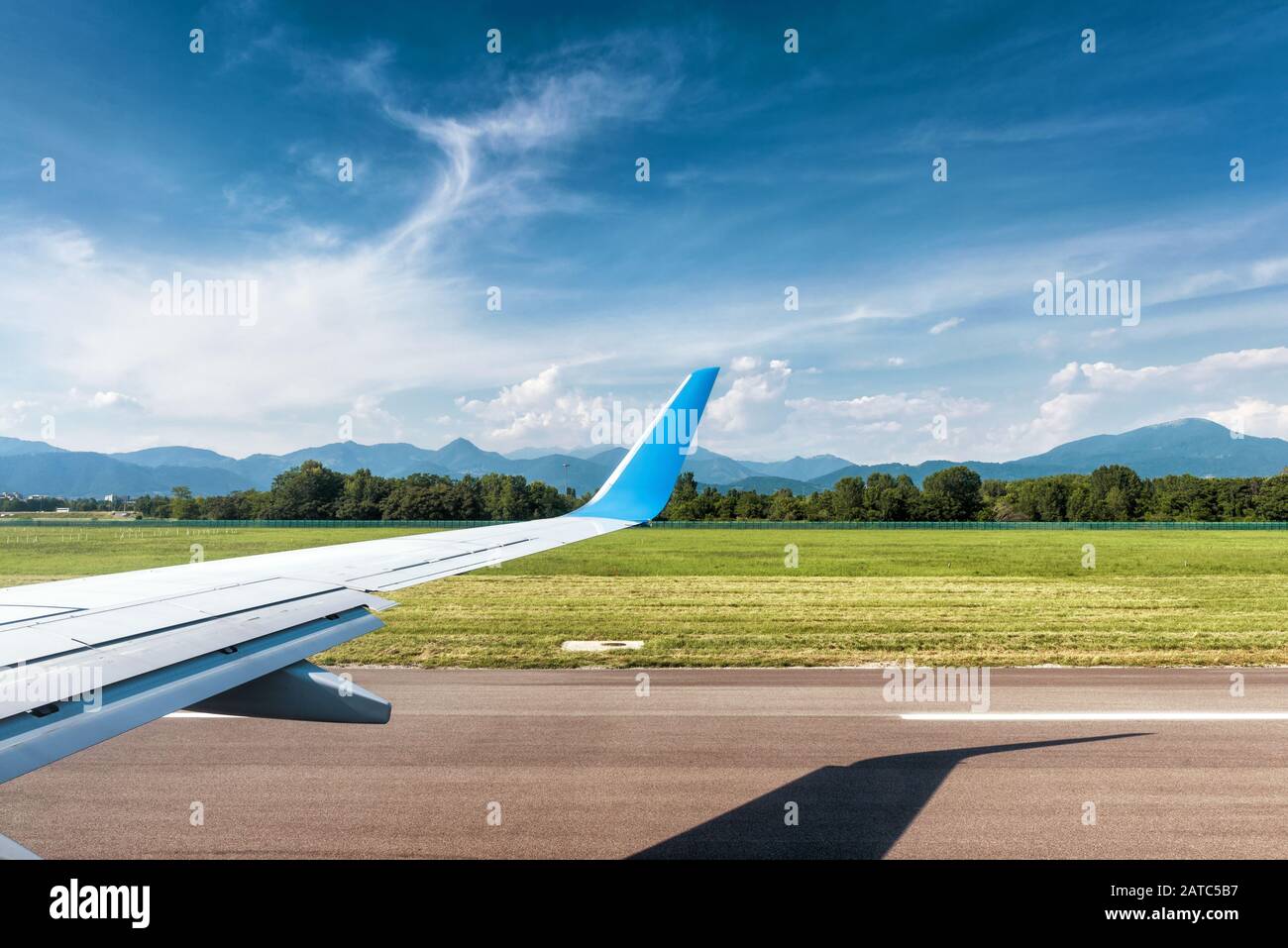 Wing of plane in Bergamo airport. Airplane is on runway. The plane takes off or landing. Arrival or departure of the airplane. Wing of airplane runnin Stock Photo
