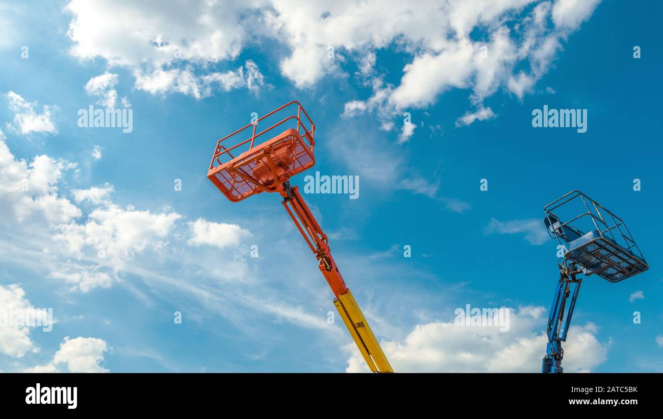Cherry pickers on blue sky background. Boom with lift buckets of heavy machinery. Panorama of the platforms of the telescopic construction lifts in su Stock Photo