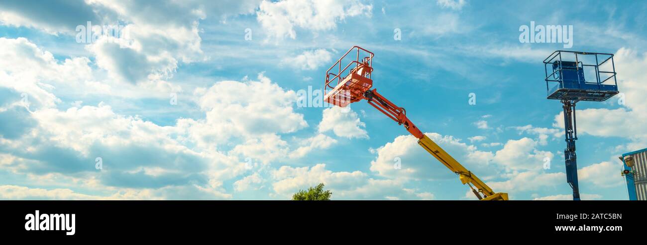 Cherry pickers on blue sky background. Boom with lift buckets of heavy machinery. Panoramic view of the platforms of the telescopic construction lifts Stock Photo