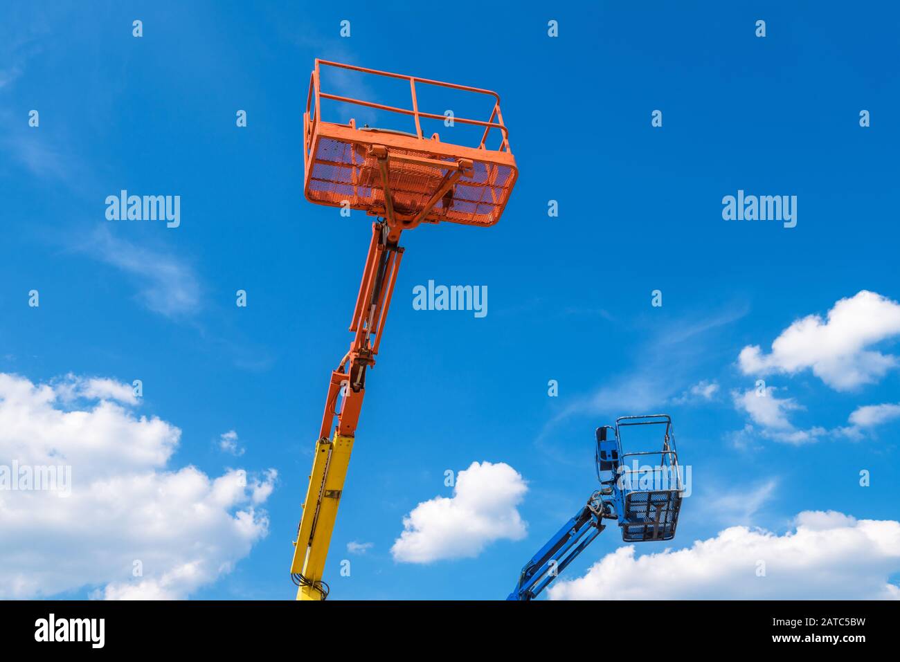 Cherry pickers on blue sky background. Boom with lift buckets of heavy machinery. Platforms of the telescopic construction lifts in summer. Stock Photo