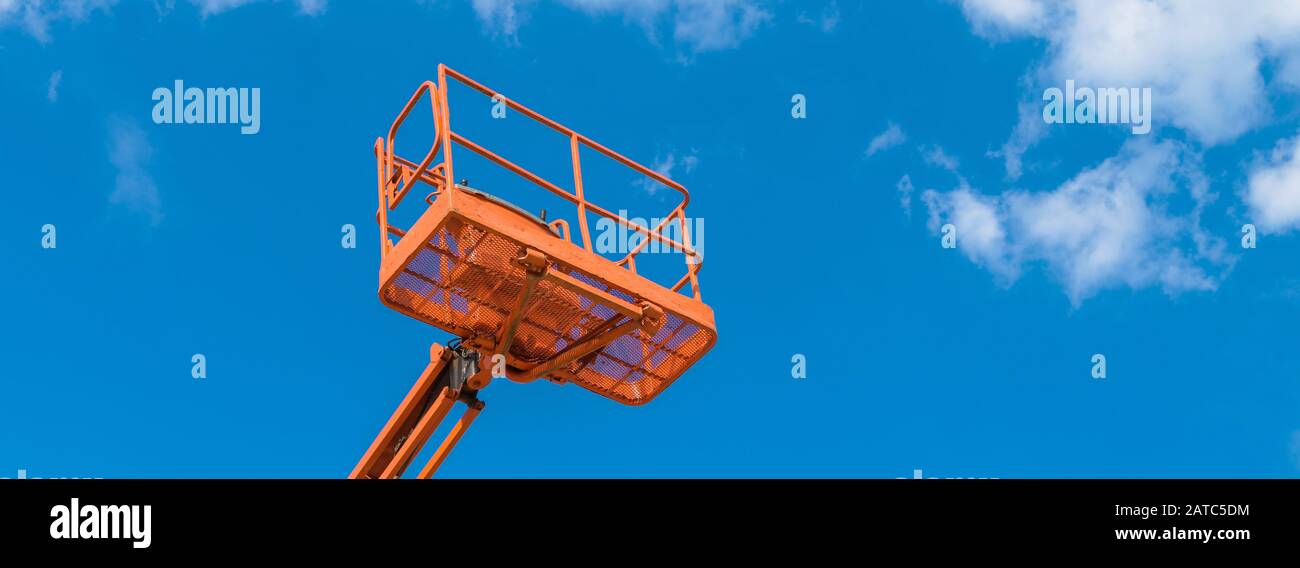 Cherry picker on blue sky background. Boom with lift bucket of heavy machinery. Platform of the telescopic construction lift close-up. Stock Photo
