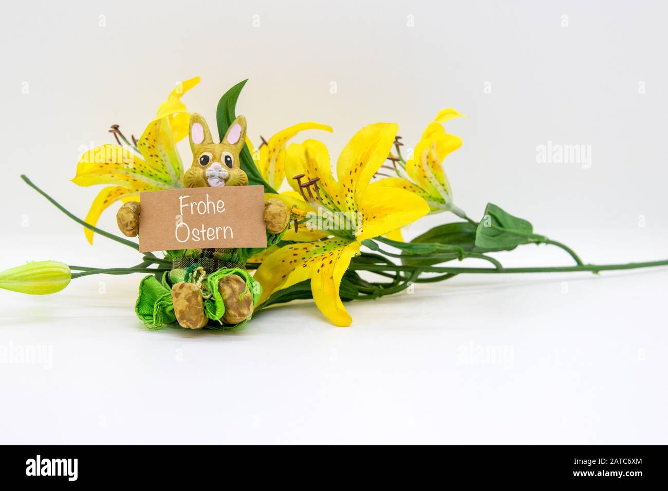 Frohe Ostern written on a sign, held by a bunny with a flower isolated on white background Stock Photo