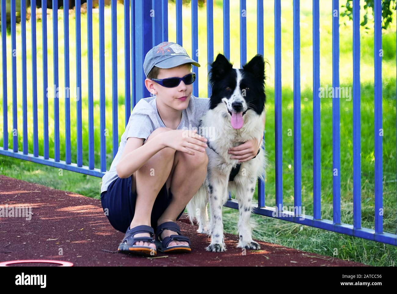 A boy in dark glasses is squatting next to a dog . Stock Photo