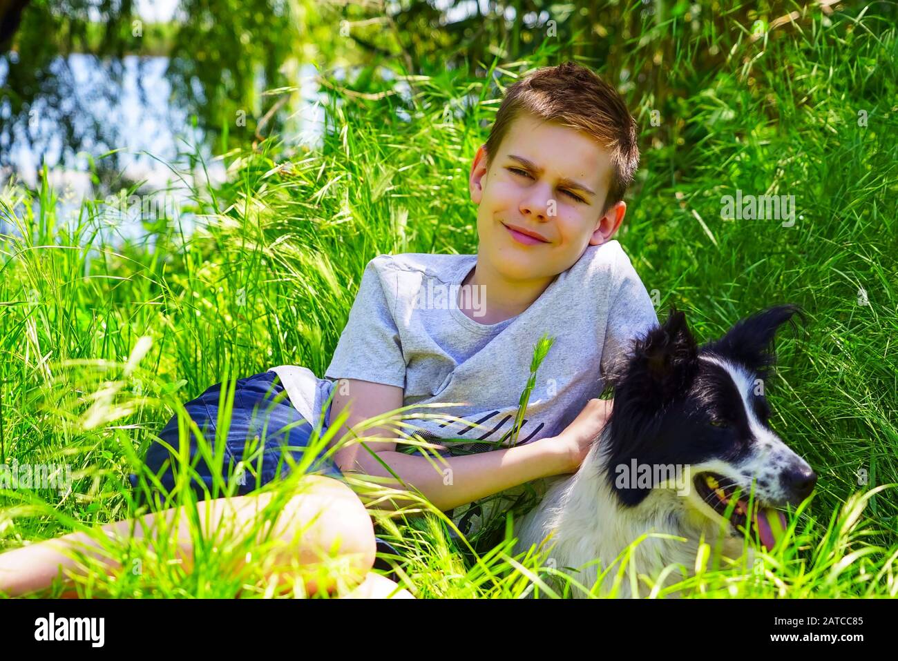 A boy sits on a green lawn and hugs a dog Stock Photo
