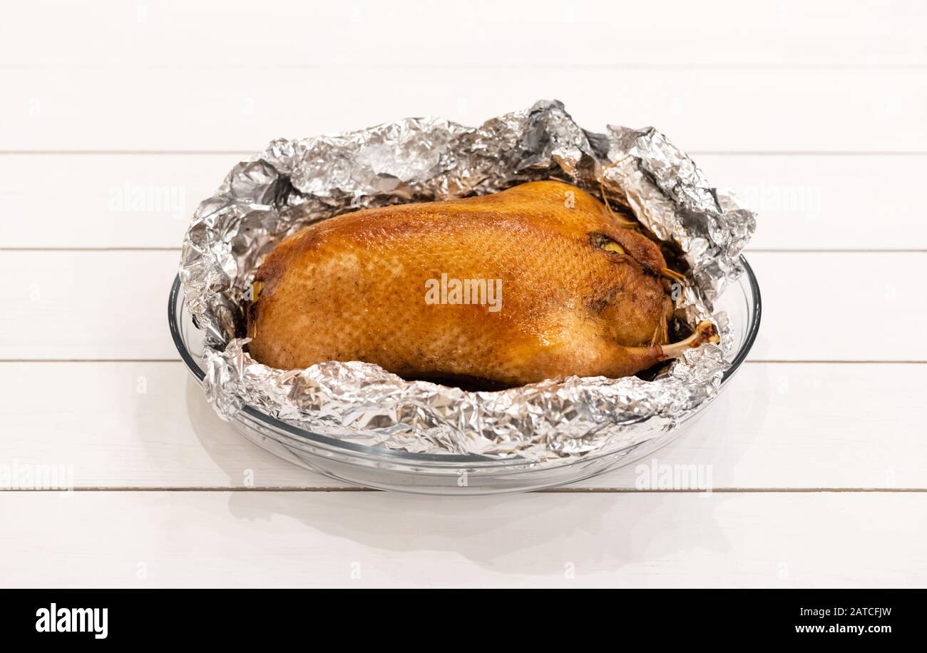 Food in foil. Duck with apples baked in foil on a white wooden background. Delicious poultry meat with a golden crust. Side view. Stock Photo