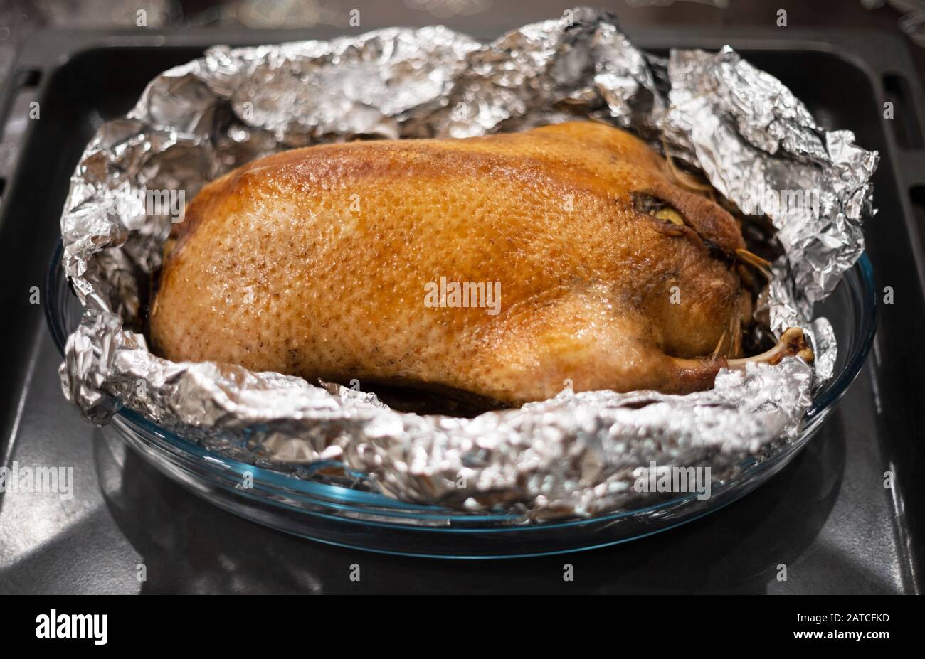 Food in foil. Duck with apples baked in foil on a tray. Delicious poultry meat with a golden crust. Side view. Stock Photo
