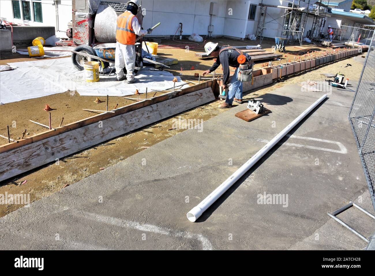 Workers putting in forms for cement curbing at public school in San Luis Obispo with full safety gear and helmets and boots Stock Photo
