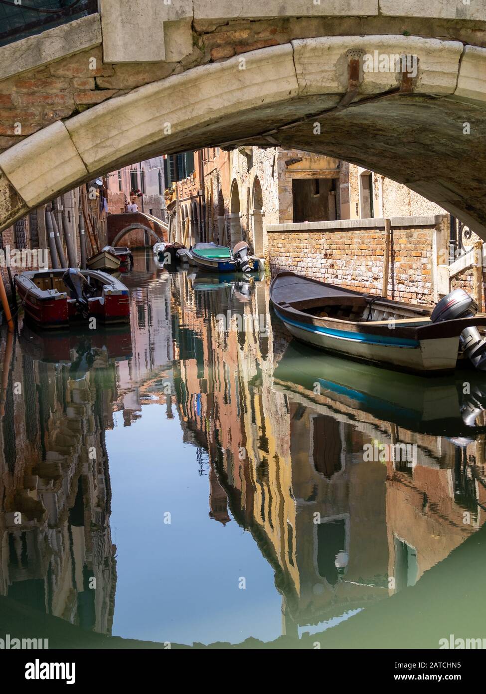Boats reflecting in the canal waters seen below a bridge, Venice Stock Photo