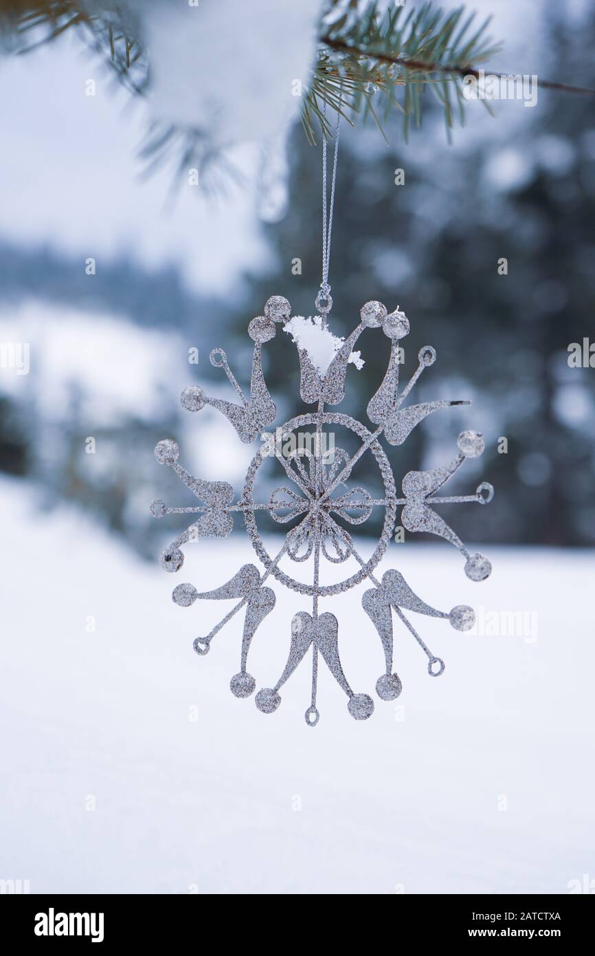 Snowflake shaped Christmas ornament hangs on the snow covered branch of a fir tree Stock Photo