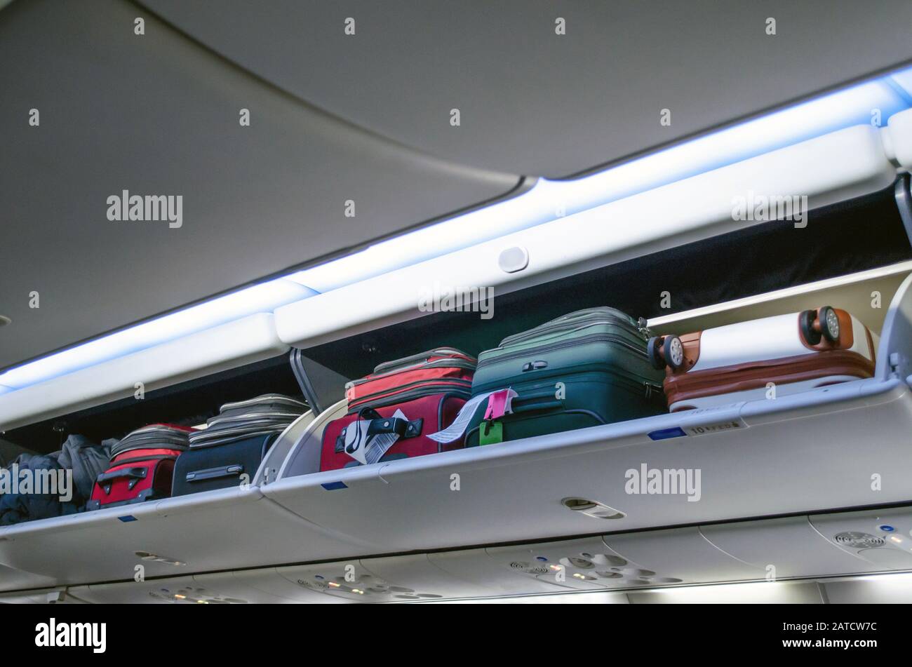 overhead bin on a airplane full of carry on bags and luggage Stock Photo