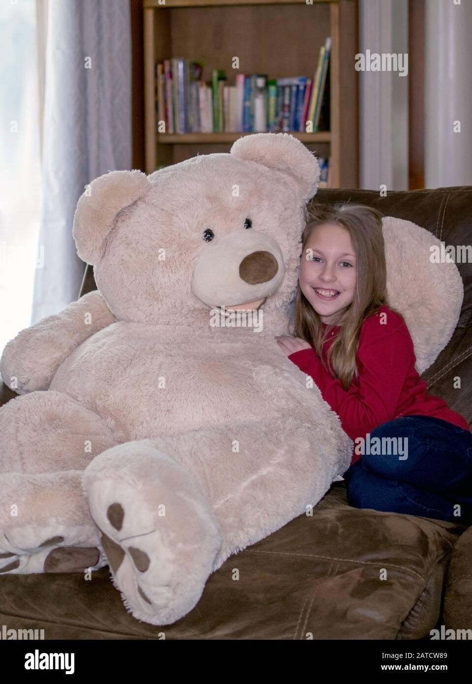 Girl cuddles with a giant teddy bear on the sofa Stock Photo
