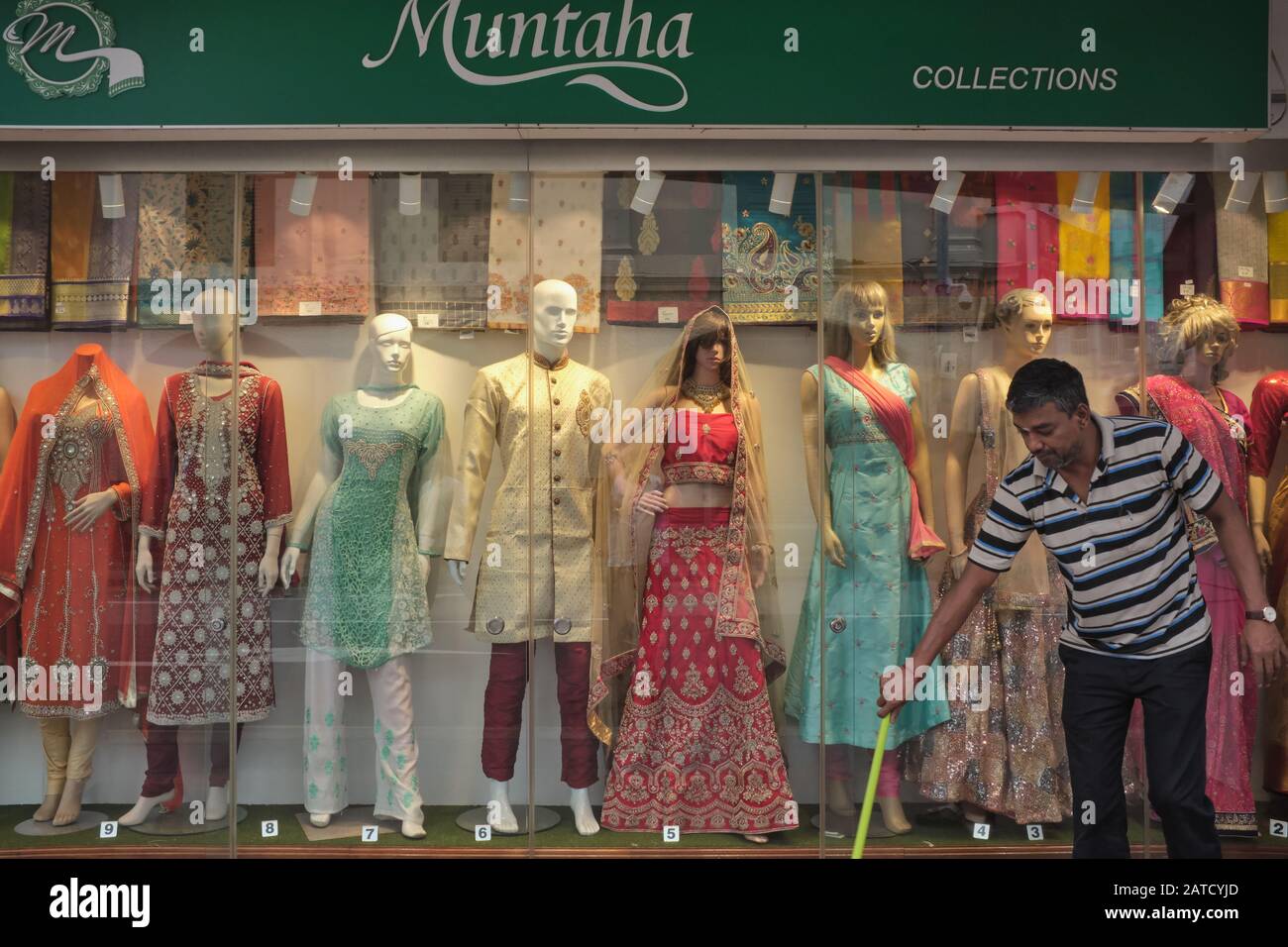 An ethnic Indian shop assistant sweeps the sidewalk in front of a shop selling Indian traditional attire; Little India area, Singapore Stock Photo