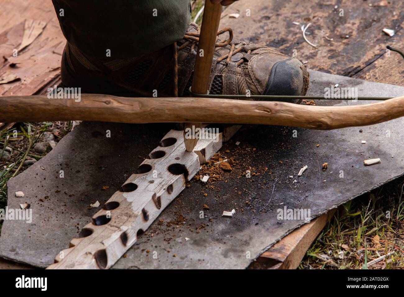 Closeup of leg of man holding wooden piece with burnt holes while demonstrating method to light fire using traditional native method during festival Stock Photo