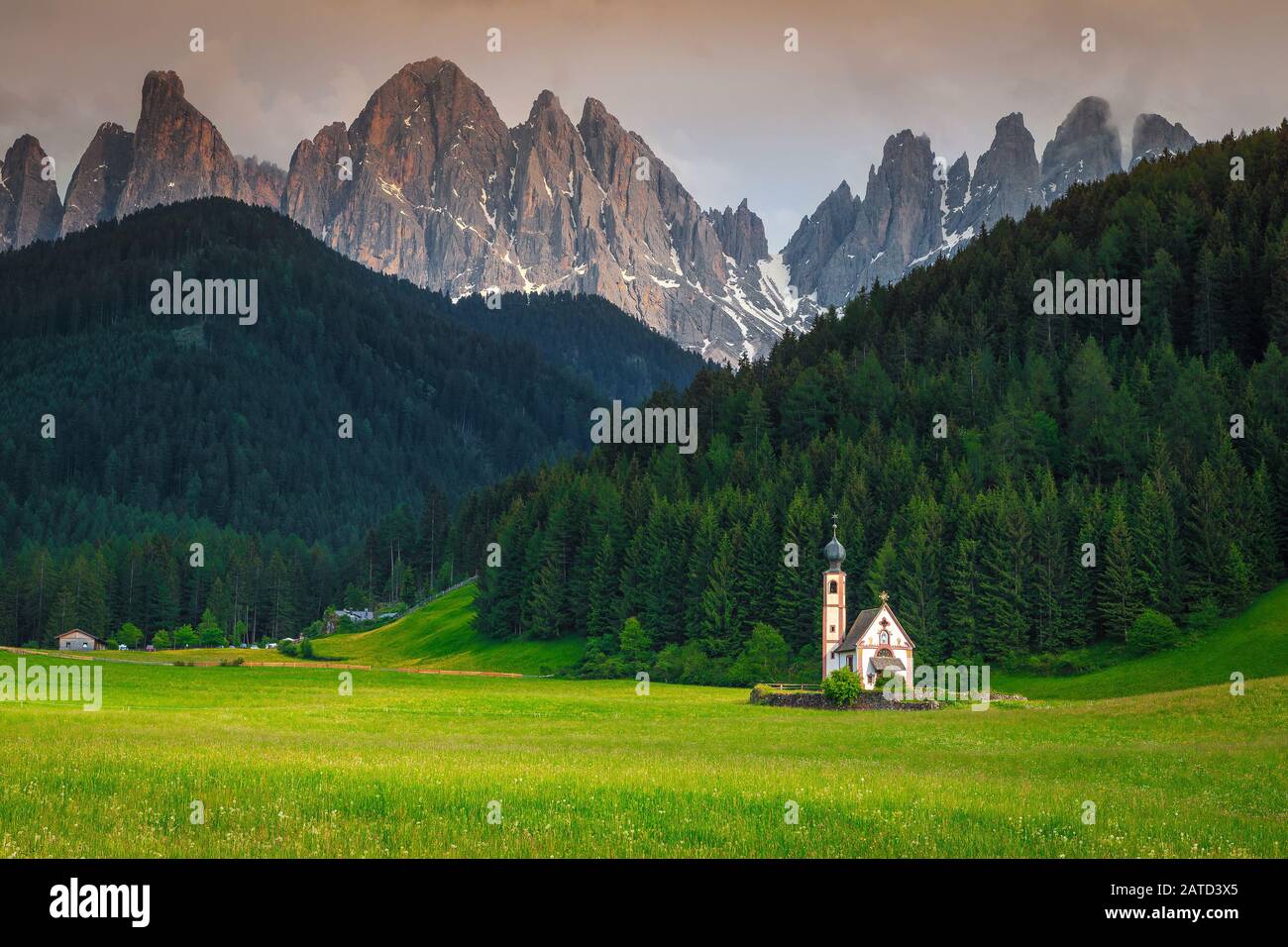 Popular travel location, cute alpine St Johann church in Val di Funes valley with green fields and high mountains at sunset, Santa Maddalena touristic Stock Photo