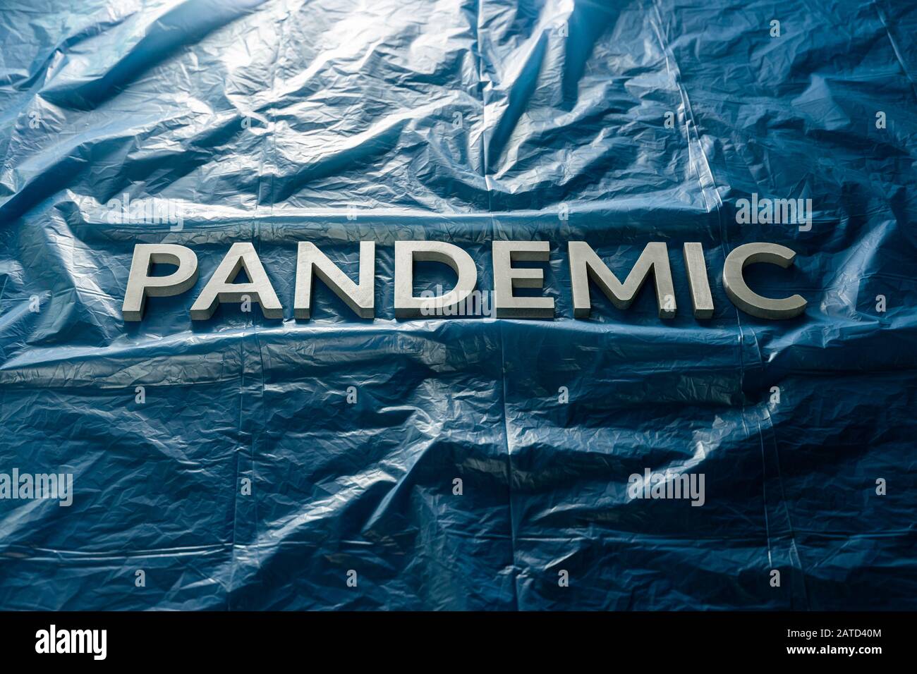 The word pandemic laid with silver letters on crumpled blue plastic film background Slanted centered with dramatic cold light. Stock Photo