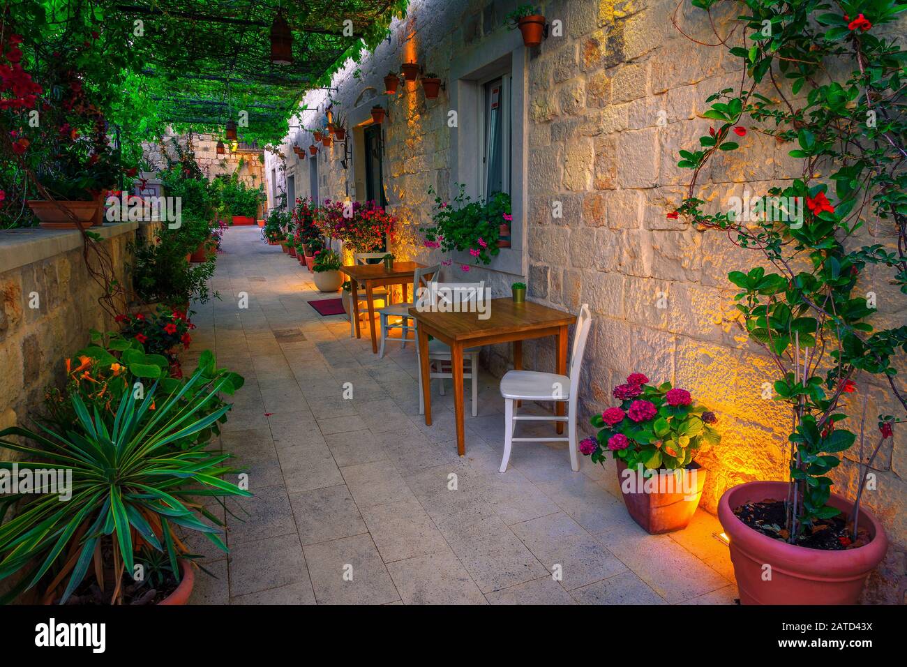 Cozy narrow street with ambiance street cafe and restaurant at morning. Flowery entrance and street lights, Hvar town, Hvar island, Dalmatia, Croatia, Stock Photo