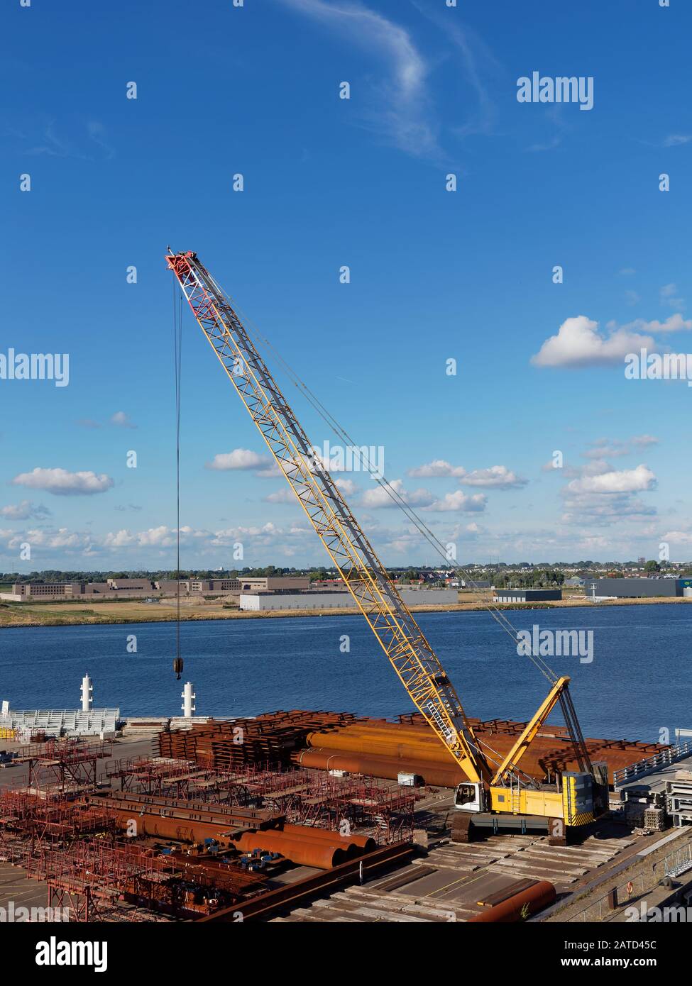 A Mobile Yellow Crane on the quayside of Alaskahaven, full of Piping, Concrete Ballast and Construction Materials. Stock Photo